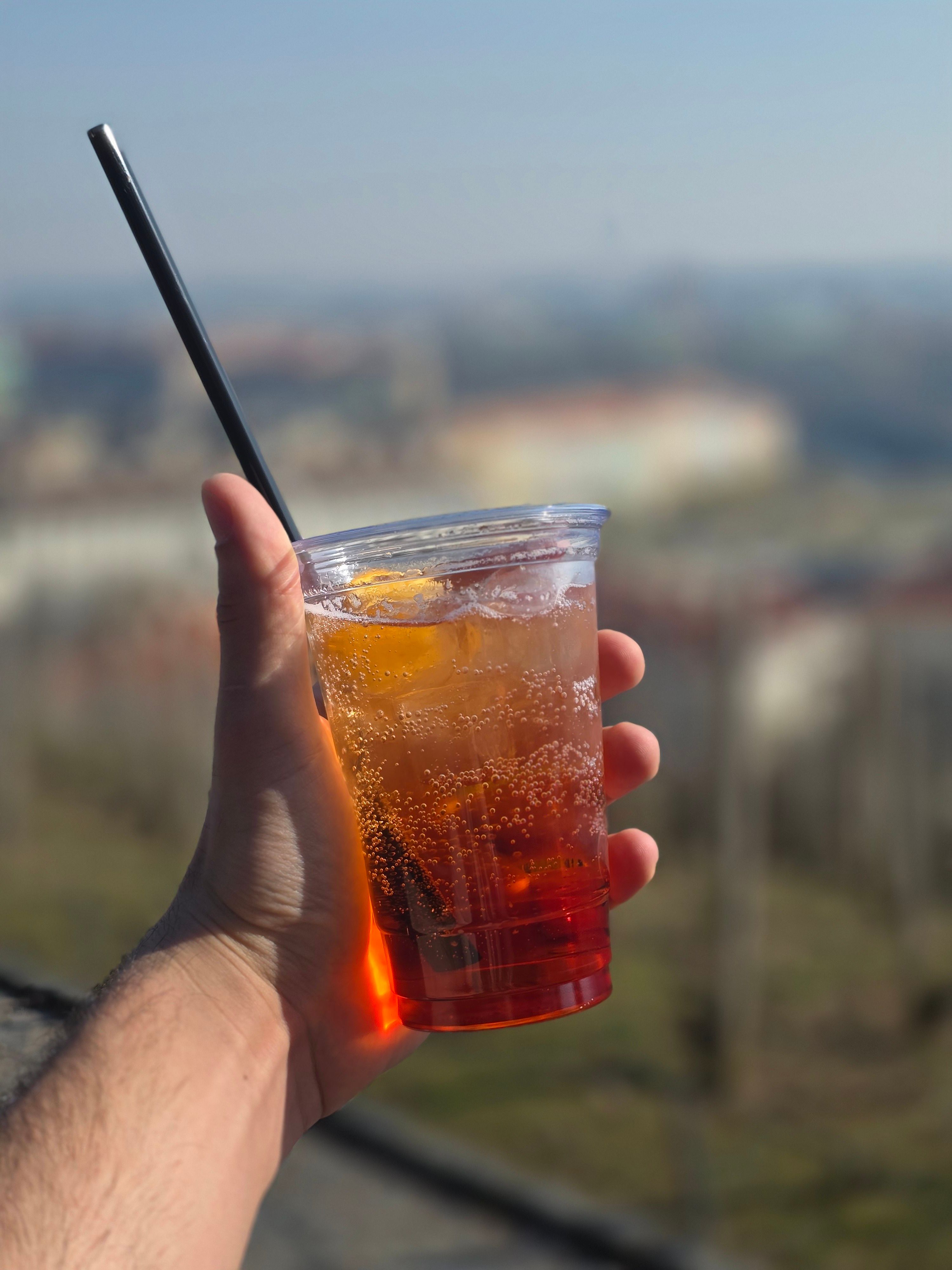 A fizzy red Americano over ice with an orange slice, held against a city view