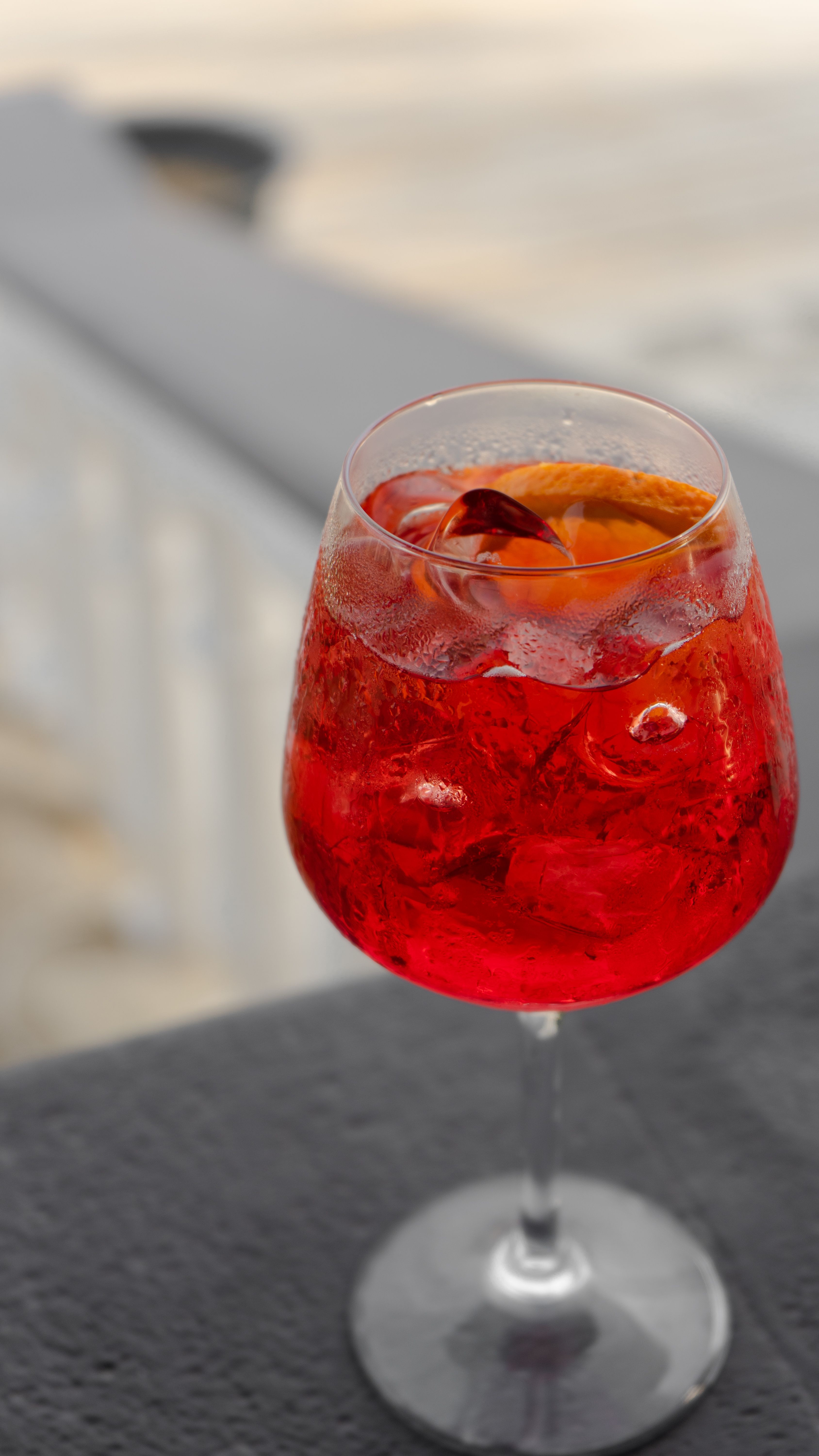 A deep-red Campari Spritz in a wine glass with orange and ice, outdoors