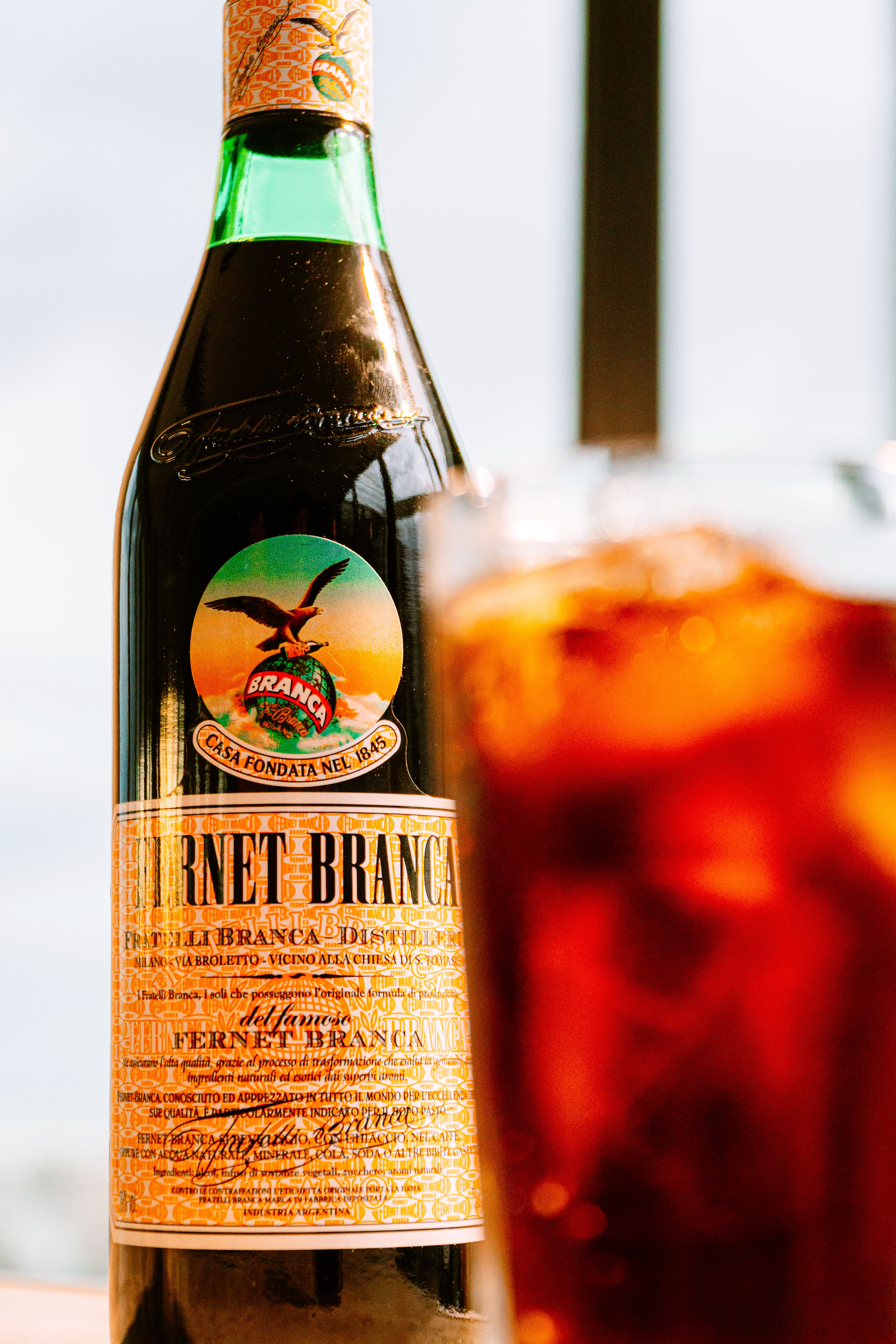 A bottle of Fernet-Branca beside a glass of the dark digestivo over ice