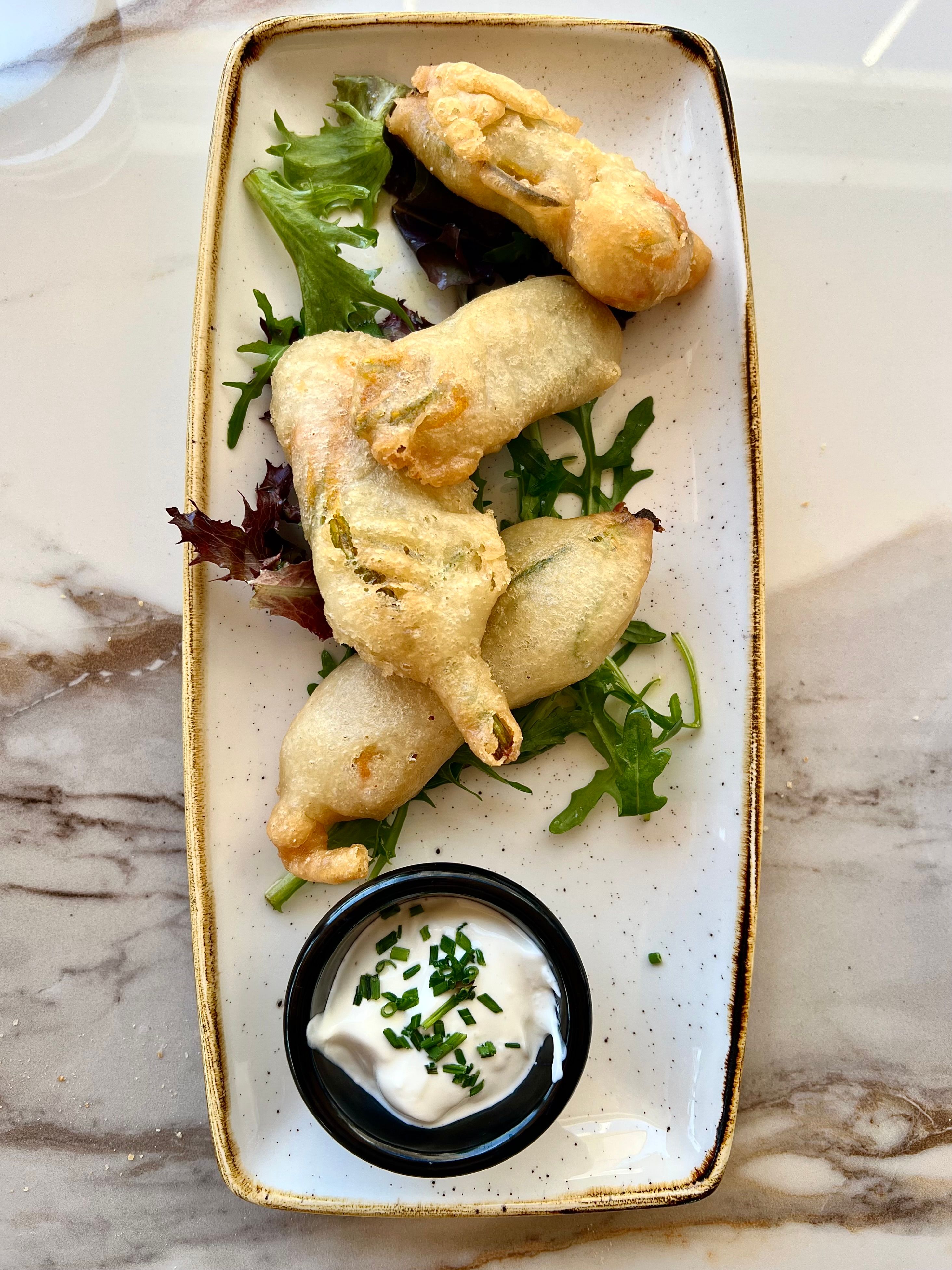 Golden battered fried courgette flowers on a plate with salad and a dip